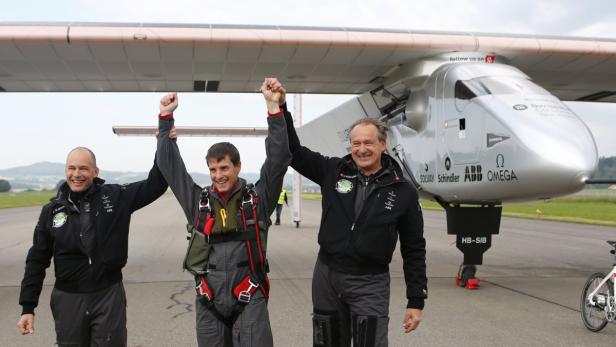 Drei Männer stehen jubelnd vor dem Solarflugzeug Solar Impulse.