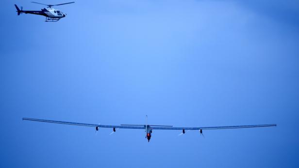 Ein Solarflugzeug und ein Hubschrauber fliegen am blauen Himmel.