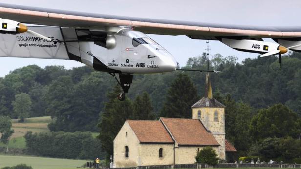 Das Solarflugzeug „Solar Impulse“ überfliegt eine Kirche auf dem Land.