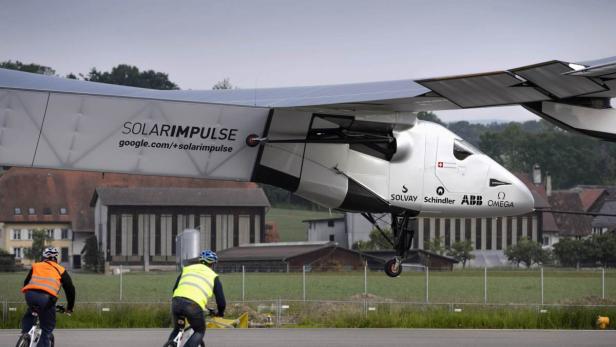 Das Solarflugzeug „Solar Impulse“ kurz vor der Landung, während zwei Radfahrer zusehen.