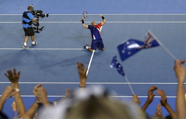 Ein Tennisspieler kniet jubelnd auf dem Platz, umgeben von australischen Flaggen.