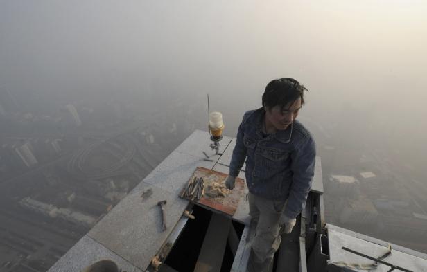 Ein Bauarbeiter steht auf dem Dach eines Wolkenkratzers in dichtem Nebel.