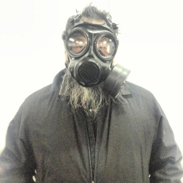 Ein Mann mit Bart trägt eine schwarze Gasmaske.