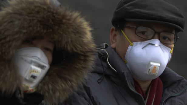 Zwei Personen tragen Atemschutzmasken und Winterkleidung.