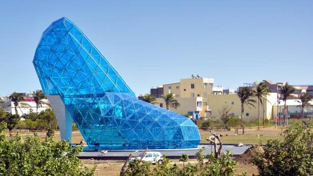 Ein riesiger, blauer Glasschuh steht in einem Park.