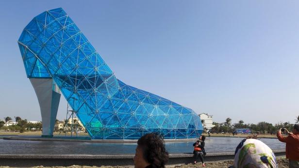 Ein riesiger, blauer Glasschuh steht in einem Park und zieht Touristen an.