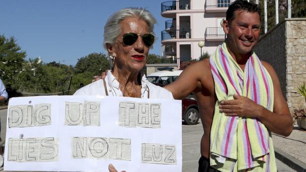 Eine ältere Frau hält ein Schild mit der Aufschrift „Dig up the lies, not Luz“ neben einem Mann mit einem Handtuch um den Hals.