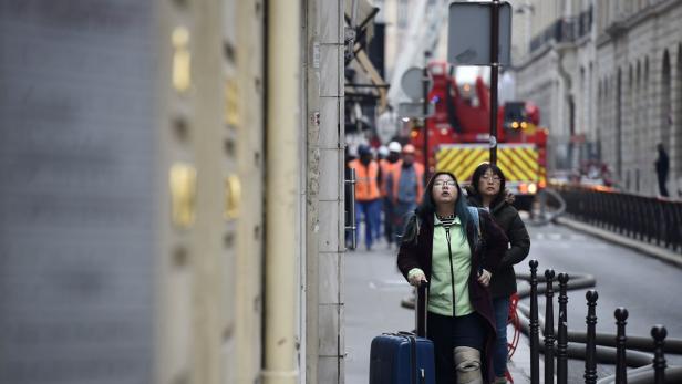Zwei Frauen stehen auf einer Straße in Paris und schauen nach oben, im Hintergrund ein Feuerwehrauto.