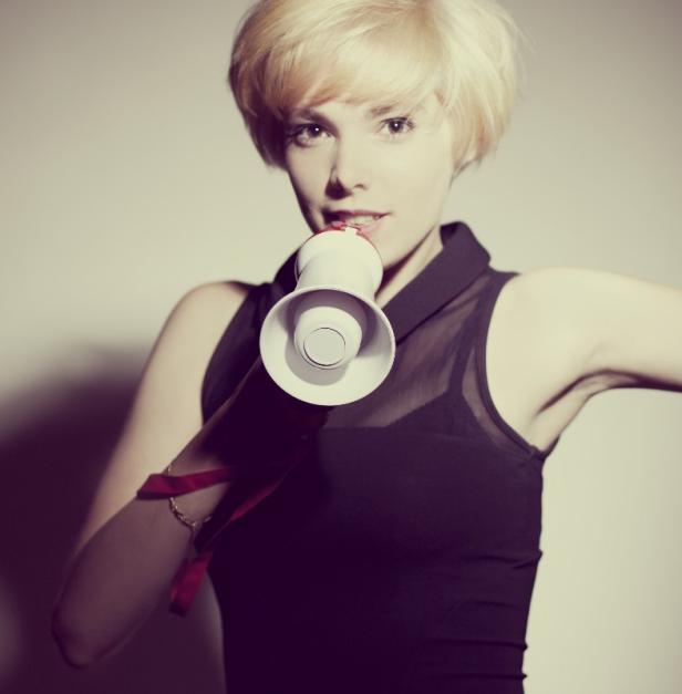 Eine Frau mit blonden Haaren spricht in ein Megafon.