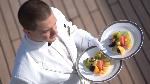 Ein Kellner im weißen Anzug serviert zwei Teller mit frischem Obst.