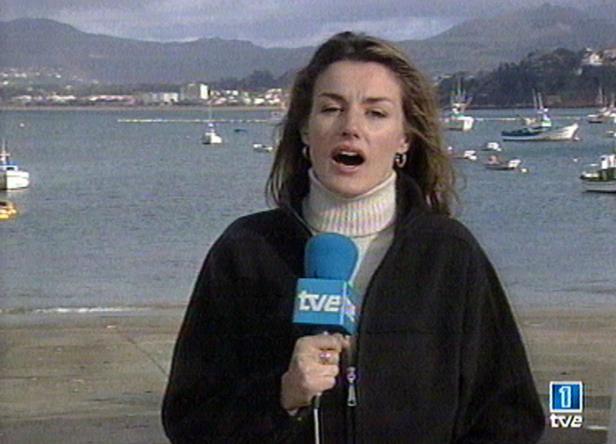 Eine TVE-Reporterin berichtet vor einer Küstenlandschaft mit Booten.