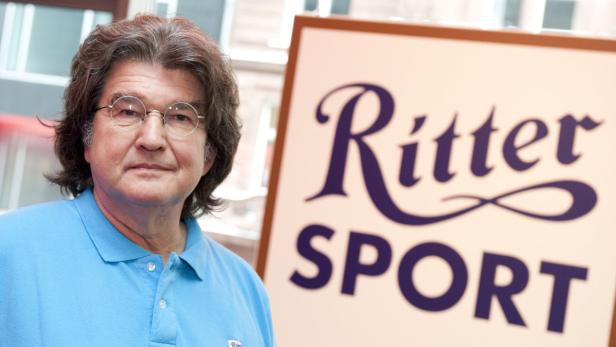 Ein Mann mit Brille steht vor einem Schild von Ritter Sport.