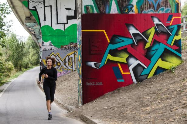 Eine Frau joggt auf einem Weg unter einer Brücke mit Graffiti.