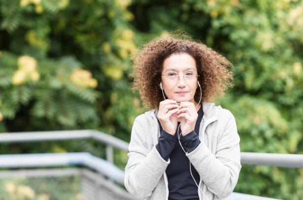 Eine Frau mit Brille und Kopfhörern steht vor einem grünen Hintergrund.