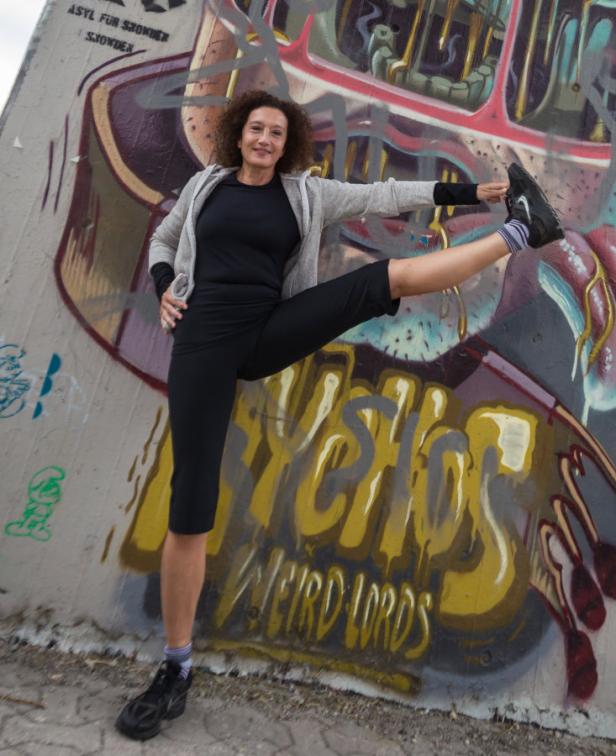 Eine Frau dehnt sich vor einer Wand mit Graffiti.