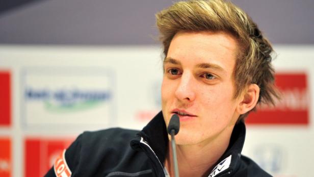 Ein junger Mann spricht in ein Mikrofon vor einem unscharfen Hintergrund.