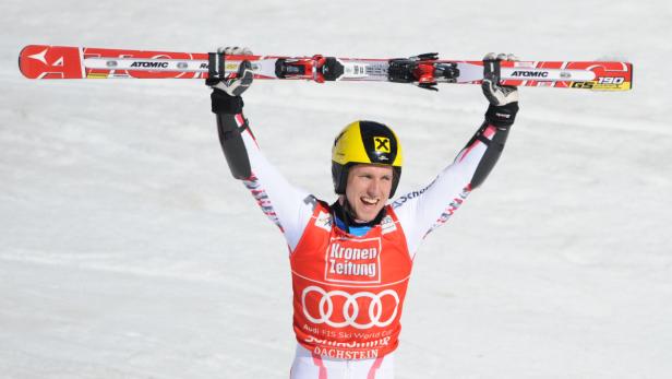 Ein Skirennläufer jubelt mit erhobenen Skiern auf einer schneebedeckten Piste.