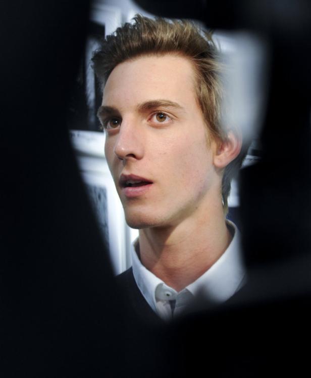 Ein junger Mann mit hellbraunen Haaren und einem weißen Hemd blickt nach oben.