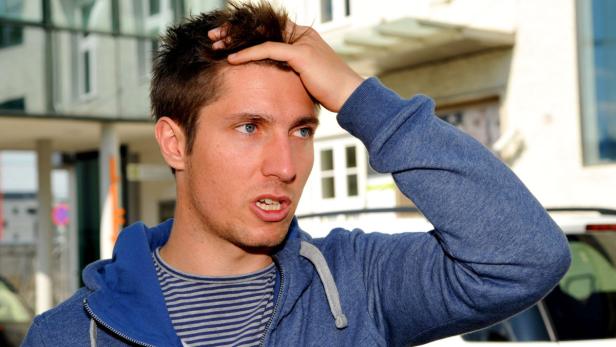 Ein Mann mit blauem Pullover und fragendem Blick hält sich an den Kopf.