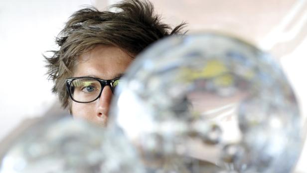 Ein Mann mit Brille schaut hinter einer glänzenden Kugel hervor.