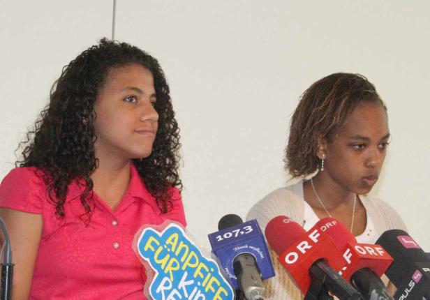 Zwei junge Frauen stehen vor Mikrofonen verschiedener Nachrichtensender.