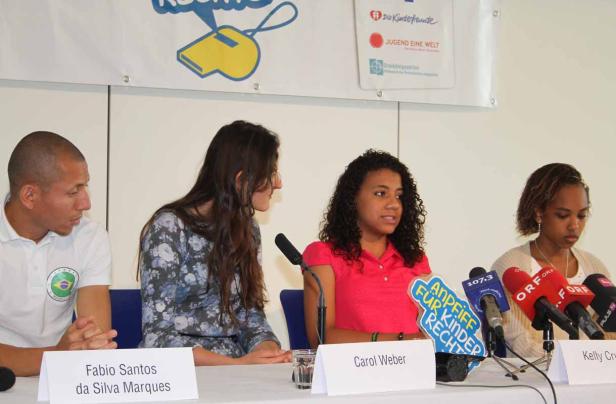 Fabio Santos da Silva Marques, Carol Weber und Kelly C. sitzen an einem Tisch mit Mikrofonen.