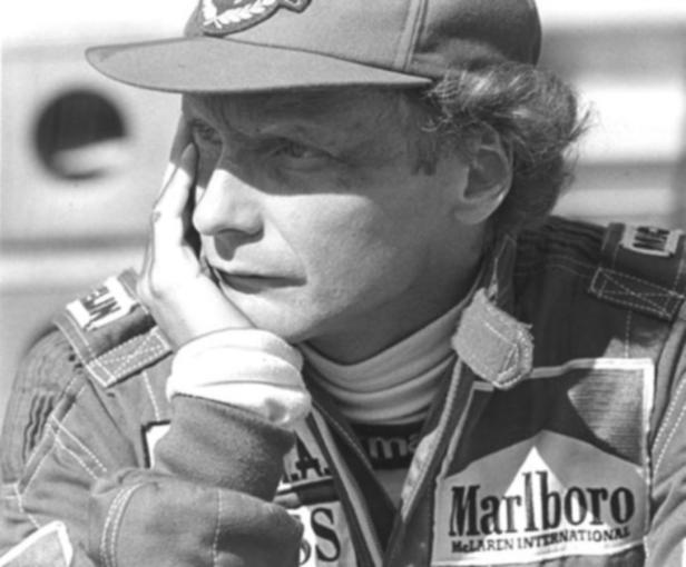 Niki Lauda in Rennfahrerkluft mit Marlboro-Logo und nachdenklichem Gesichtsausdruck.
