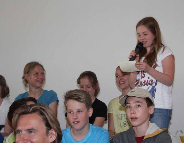 Ein junges Mädchen liest vor einer Gruppe von Zuhörern von einem Blatt Papier in ein Mikrofon.