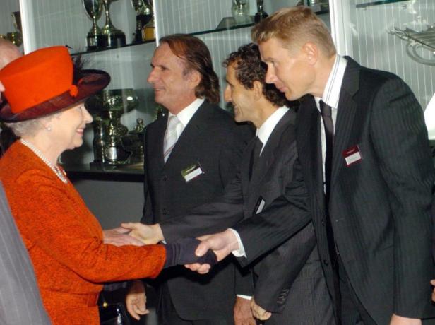 Königin Elisabeth II. schüttelt einem Mann die Hand, während zwei weitere Männer zusehen.