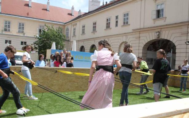 Kinder spielen mit Gummibändern auf einer Wiese vor einem Gebäude.