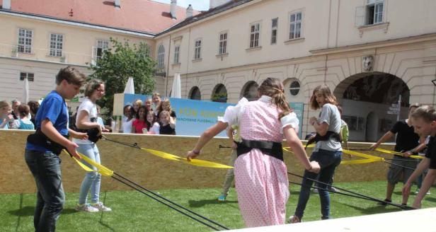 Kinder spielen mit einem Gummibandspiel im Freien vor einem Gebäude.