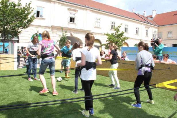 Eine Gruppe Kinder spielt ein Spiel mit Gummibändern auf einer Rasenfläche.
