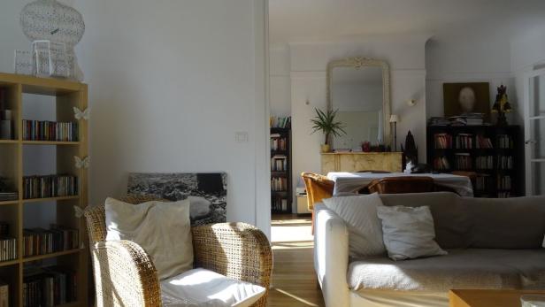 Ein Wohnzimmer mit Bücherregalen, einem Sofa und einem Korbsessel.