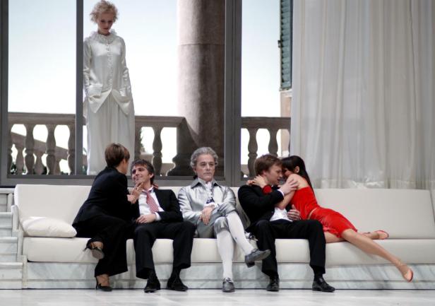 Szene aus einem Theaterstück mit mehreren Darstellern auf einer weißen Couch.