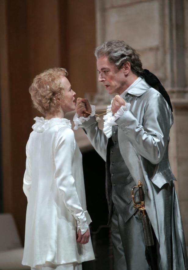 Ein Mann im Kostüm hält einer Frau eine Halskette vor das Gesicht.