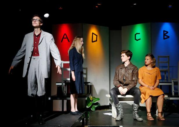 Vier Schauspieler stehen auf einer Bühne vor farbig beleuchteten Buchstaben.