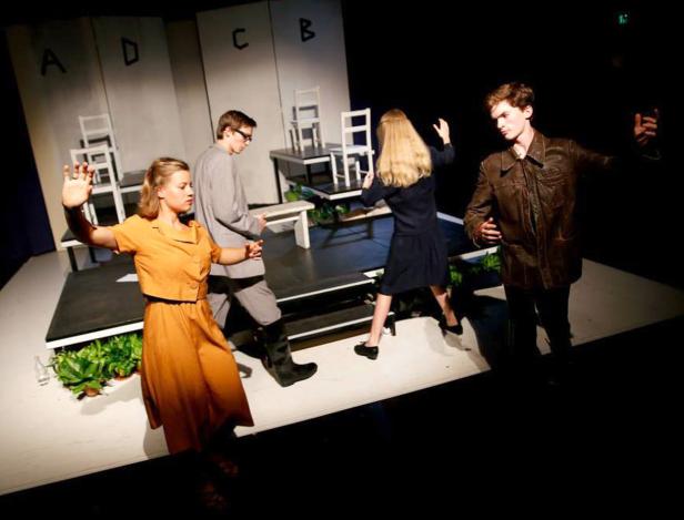 Vier Schauspieler stehen auf einer Bühne vor einem minimalistischen Bühnenbild.