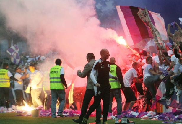 Fußballfans zünden Pyrotechnik und schwenken Fahnen im Stadion.