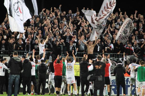 Fußballfans jubeln mit Fahnen und erhobenen Händen auf der Tribüne.