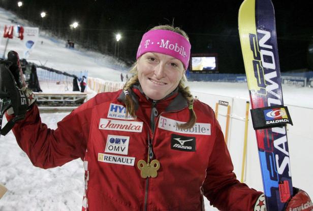 Eine Skirennläuferin mit Skiern und Sponsorenlogos auf ihrer Jacke.