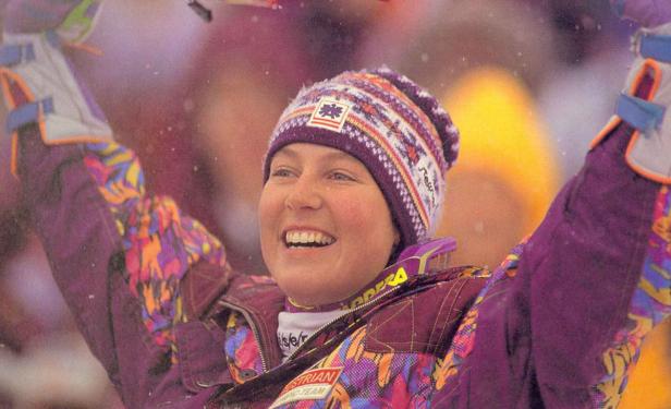 Eine jubelnde Skifahrerin mit Mütze und farbenfroher Jacke.