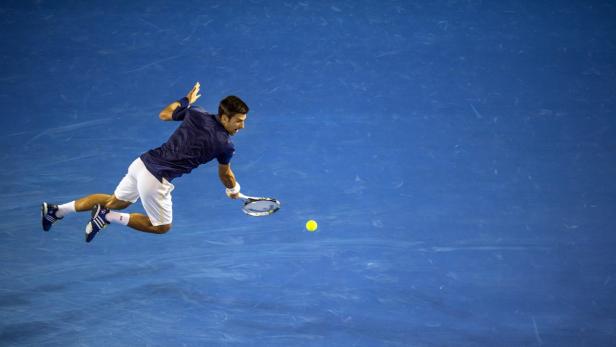 Novak Đoković schlägt einen Tennisball auf einem blauen Platz.