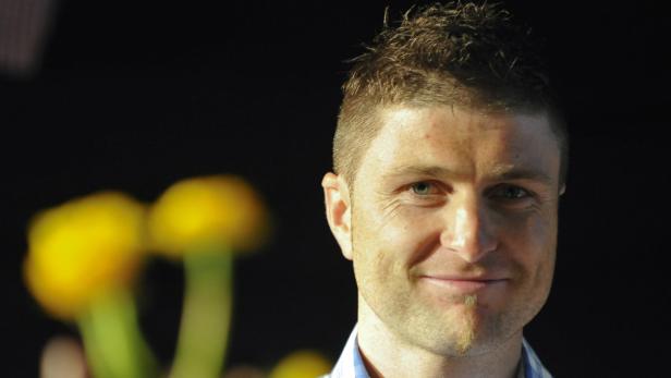 Ein Mann mit kurzem, dunklem Haar lächelt in die Kamera.