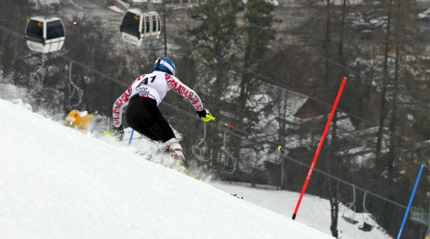 Ein Skifahrer fährt einen schneebedeckten Hang hinunter, im Hintergrund eine Seilbahn.