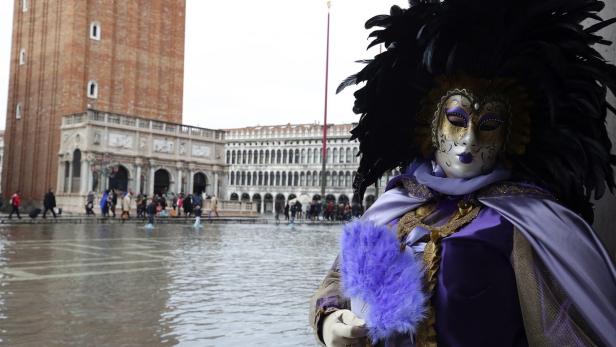 Eine Person in venezianischer Karnevalstracht steht auf dem überfluteten Markusplatz.