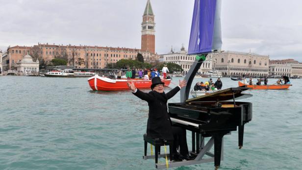 Ein Mann mit Zylinder spielt Klavier auf einem schwimmenden Floß in Venedig.