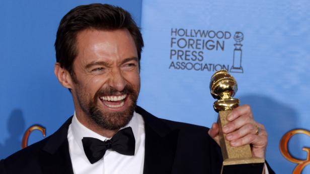 Hugh Jackman lacht und hält einen Golden Globe Award in der Hand.