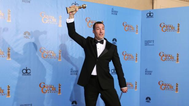 Ein Mann im Smoking hält eine Golden Globe-Trophäe in die Höhe.