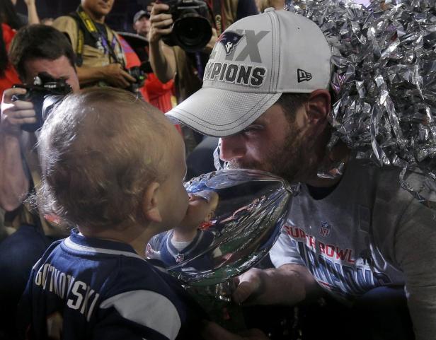 Ein Mann und ein Baby küssen die Vince Lombardi Trophy nach dem Super Bowl.
