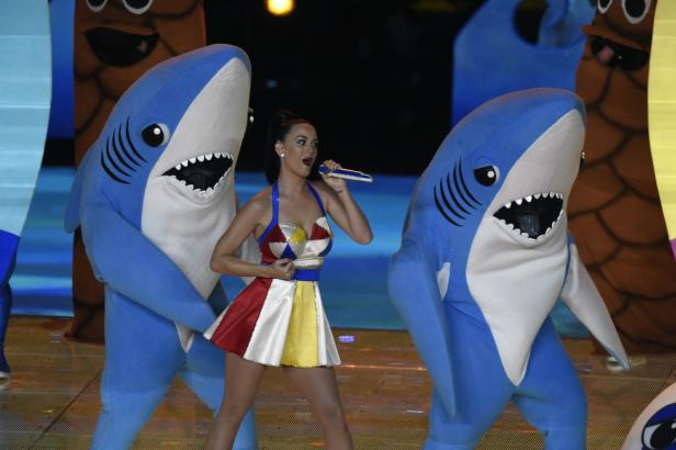 Katy Perry tritt mit zwei Tänzern in Haikostümen auf einer Bühne auf.